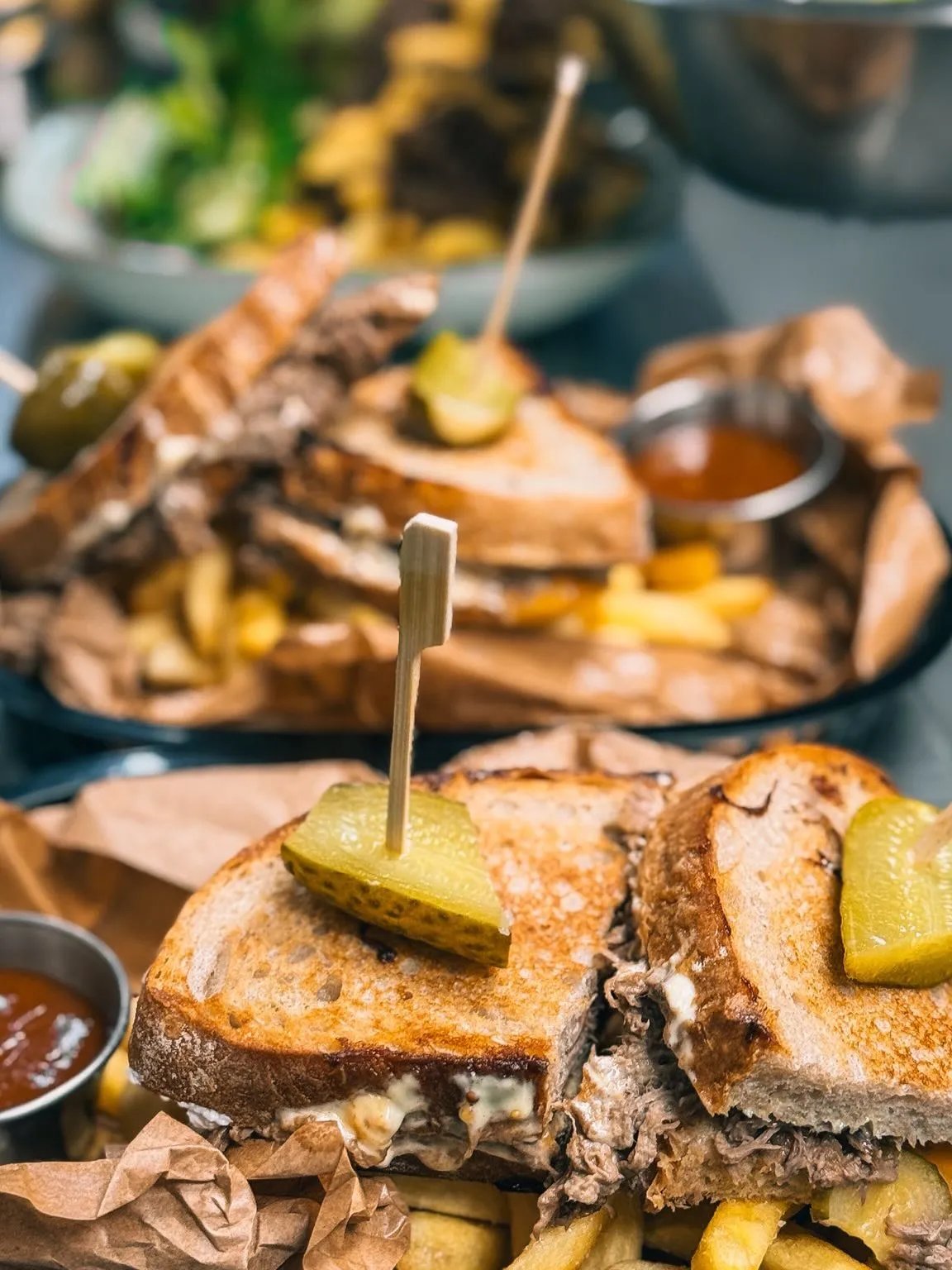 Toast s trhaným hovězím a nakládanou okurkou na kraftovém papíru, hranolky